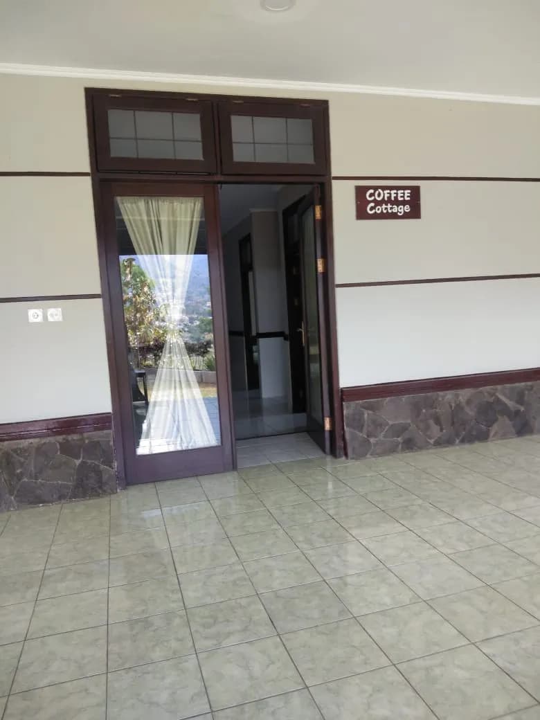 Teras Coffee Cottage berlantai keramik dengan pintu kaca terbuka dan papan nama Coffee Cottage di dinding.