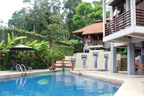 Kolam renang UTC dengan air biru, kursi berjemur di tepinya, dan bangunan kayu bertingkat di sisi kolam.