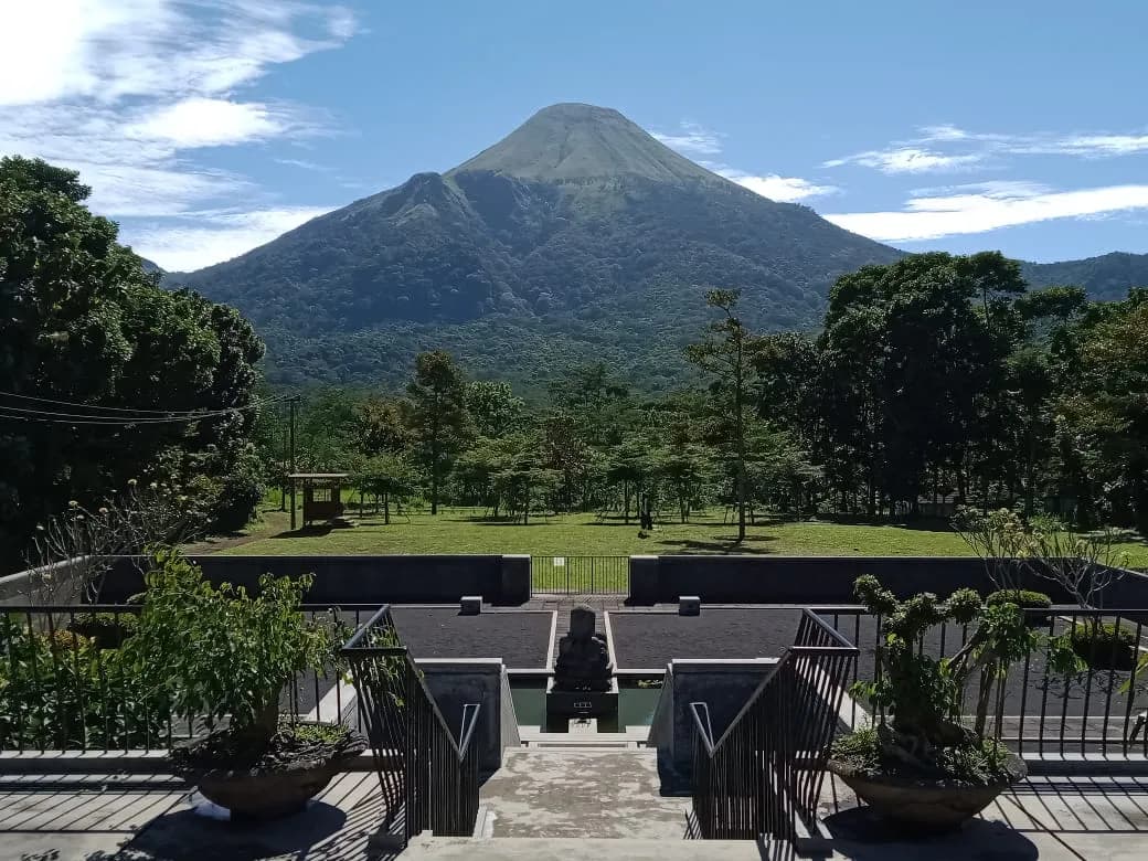 Lapangan rumput Mojopahit di kawasan UTC dengan tangga batu di latar depan dan puncak Gunung Penanggungan di kejauhan.